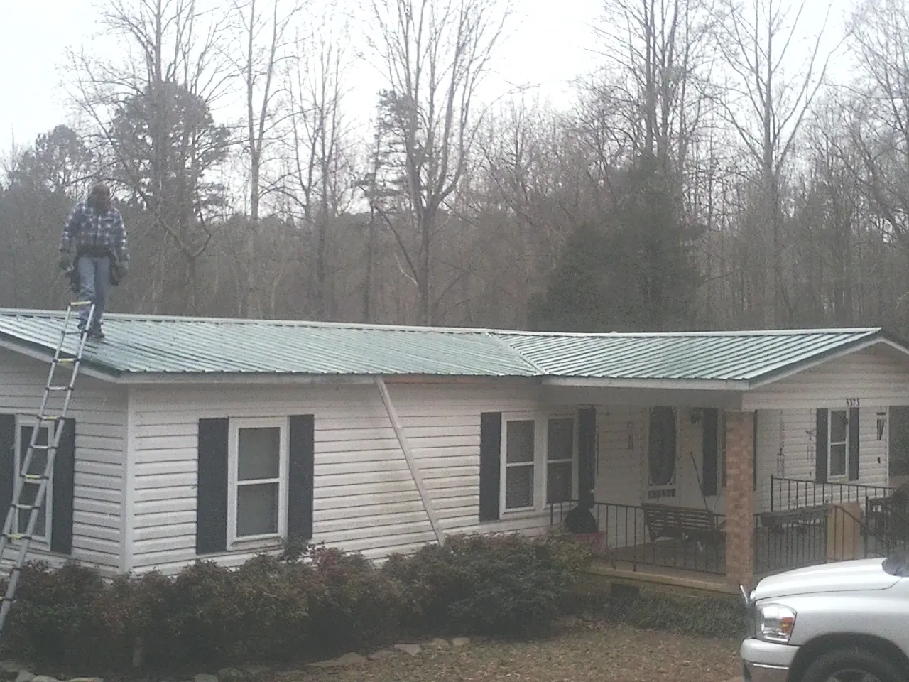 Worker on a ladder beside a new green metal roof on a ranch home in Kevil