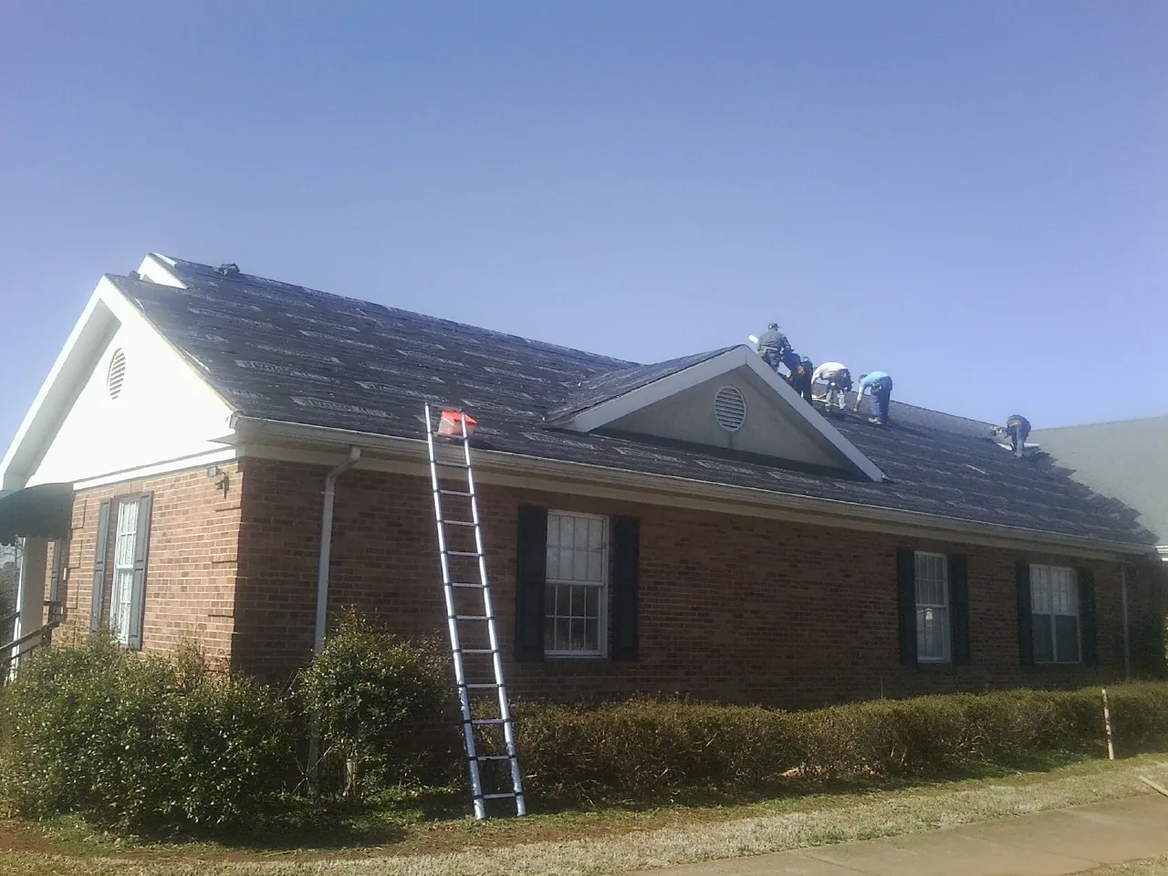 Crew tearing shingles off a brick ranch roof with a ladder set — Emergency Roof Repair work by our crew in Kevil