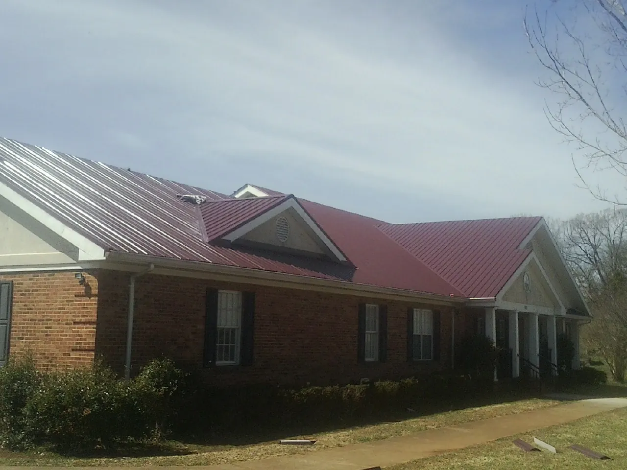 Red metal roof with gabled entries on a long brick building, from a Hail Damage Roof Repair job in Kevil