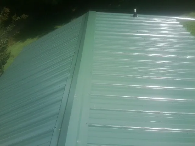 New green metal panels meeting at the ridge of a roof — Flat Roof Repair work by our crew in Kevil