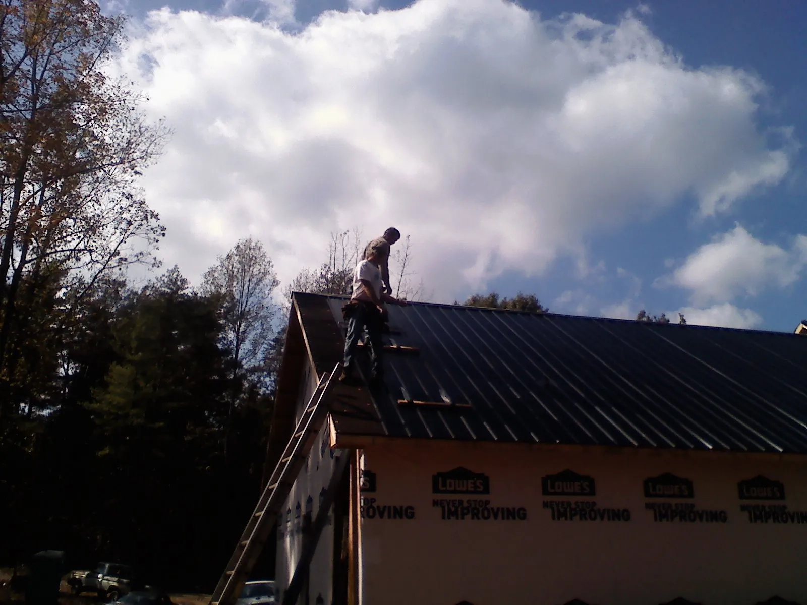 Roofer fastening dark metal panels high against a cloudy sky, from a Roof Inspection job in Kevil