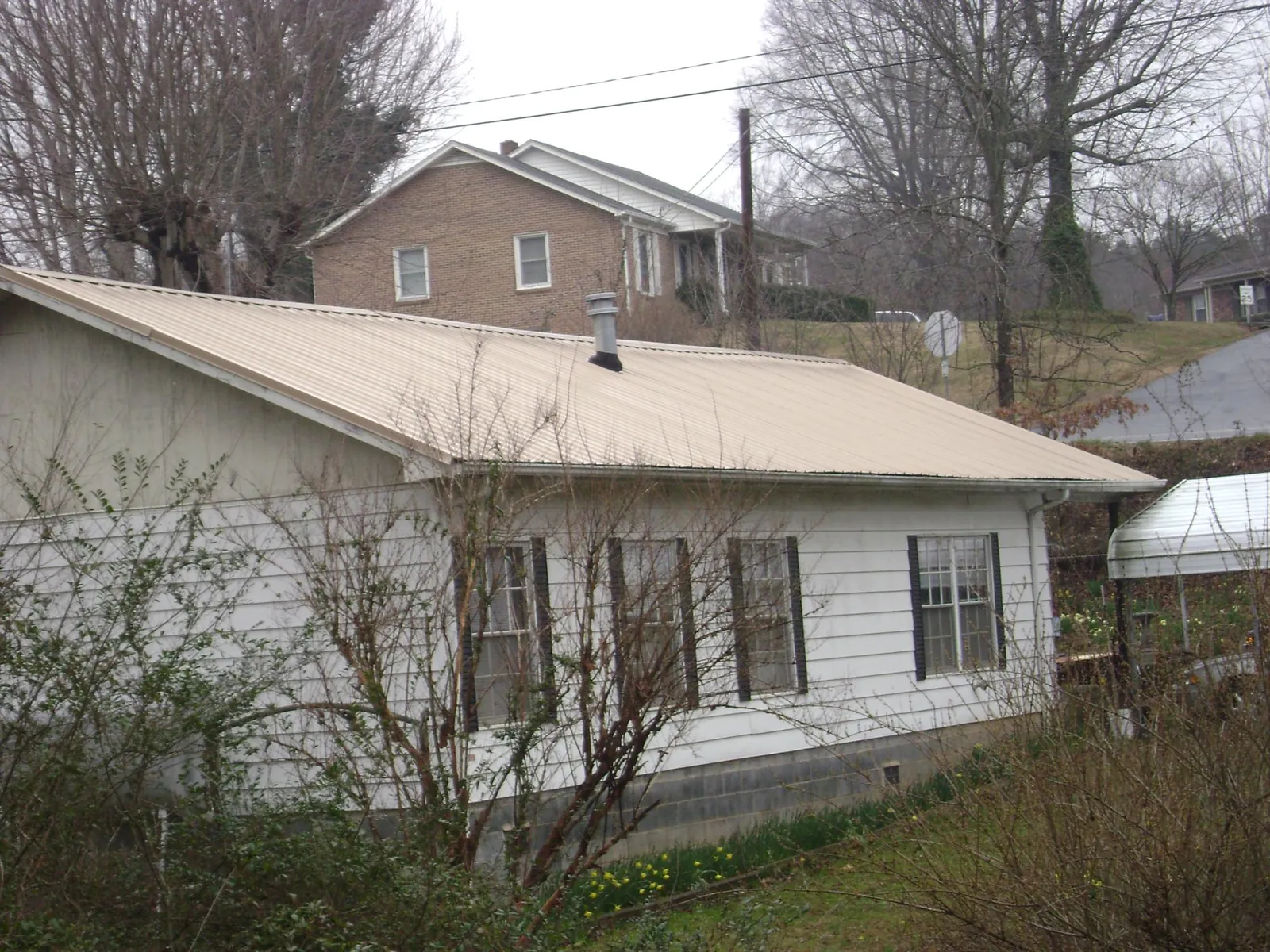 Tan metal roof on a white sided house set into a hillside — Commercial Roofing by Roofing Brothers in Kevil